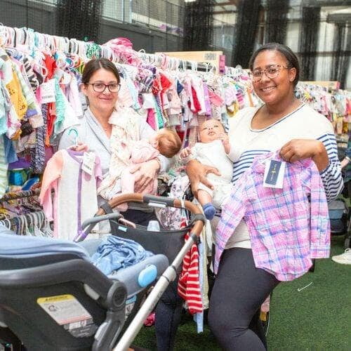 Three generations shop together at their local JBF sale. Mom carries baby in a baby carrier while grandmom stands behind them.