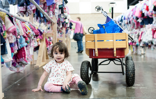 A child sits by a wagon in between two rows of little girl clothes